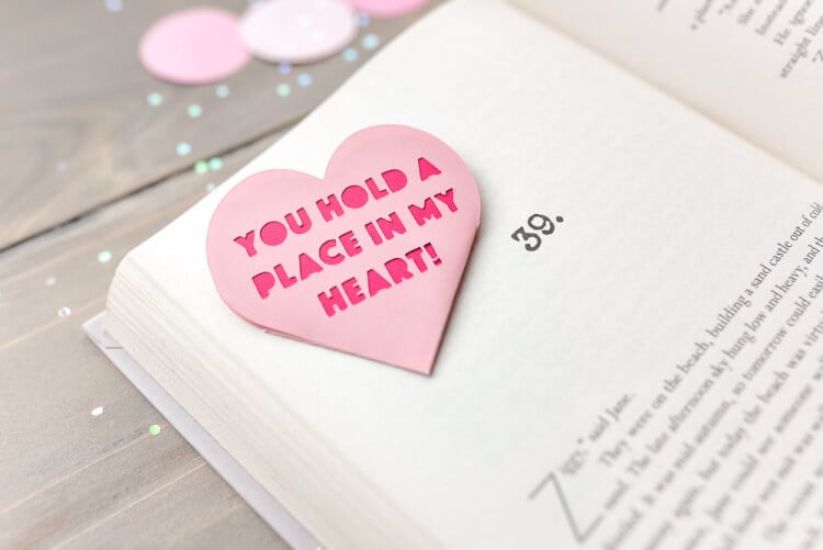 An open book lying on a table with a Valentine bookmark that says, \"You Hold a Place in my Heart!\"