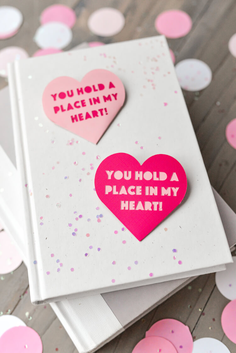 A book lying on a table with two Valentine bookmarks laying on top of it that say, \"You Hold a Place in my Heart!\"