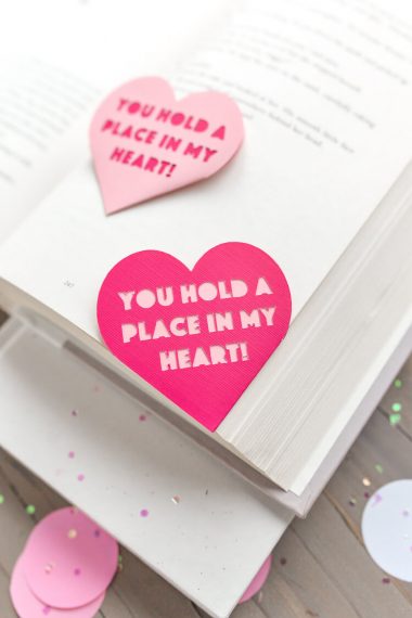 An open book lying on a table with a Valentine bookmark in the corner that says, "You Hold a Place in my Heart!"