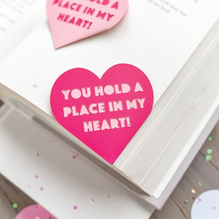 A book with a pink heart shaped bookmark that says, \"You Hold a Place in My Heart\"