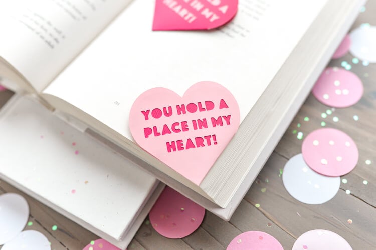 An open book lying on a table with a Valentine bookmark in the corner that says, \"You Hold a Place in my Heart!\"