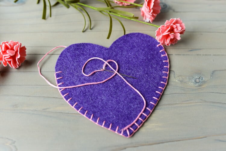 Flowers laying on a table next to a heart cut out of felt and a needle and thread