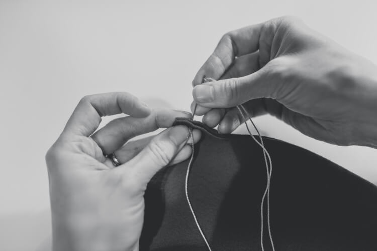 A woman\'s hands with a needle and thread sewing together two pieces of felt