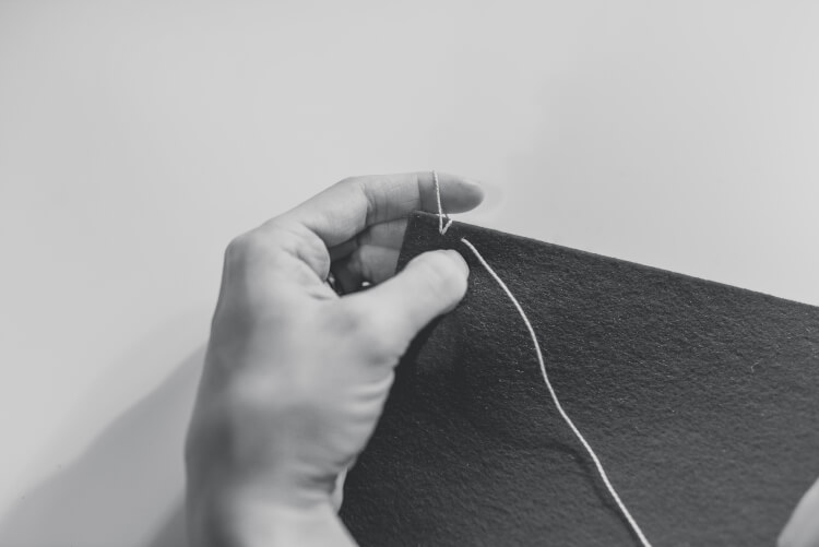 A woman\'s hands with a needle and thread sewing together two pieces of felt