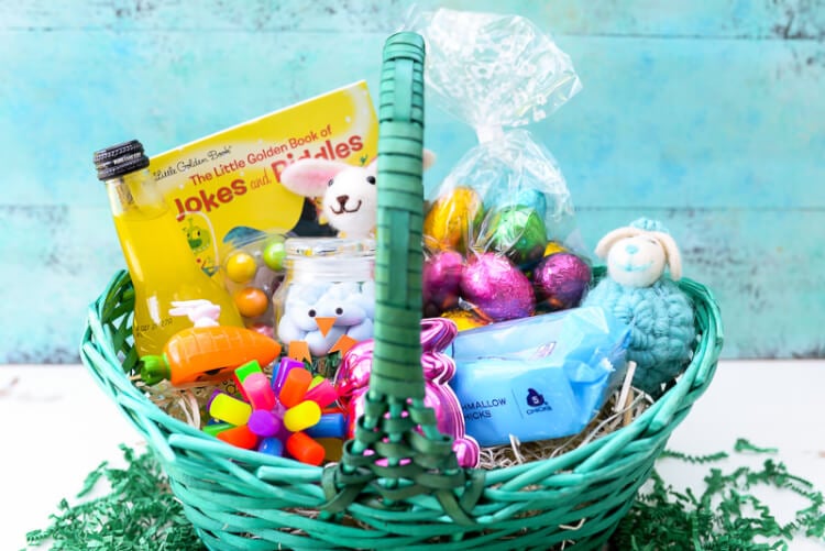 A blue green basket sitting on a table next to an aqua-colored wall.  The basket is filled with Easter candy and toys