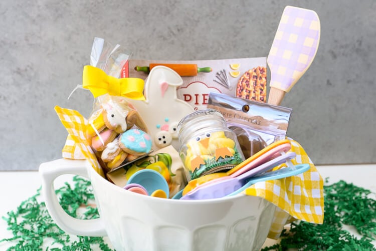 A large mixing bowl filled with measuring cups, measuring spoons, a spatula, a cookbook and other Easter items
