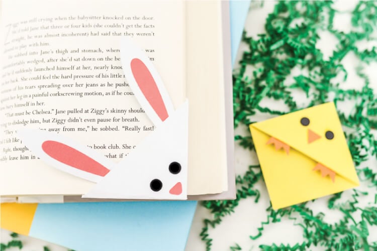 A bookmark of a bunny over the corner of a book and a chick bookmark lying next to it