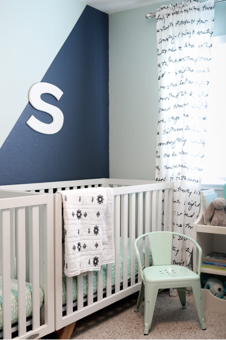 A nursery with two cribs, a mint green chair and walls painted in dark blue and mint green