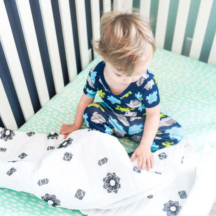 A small child wearing pajamas and sitting on a bed touching a blanket