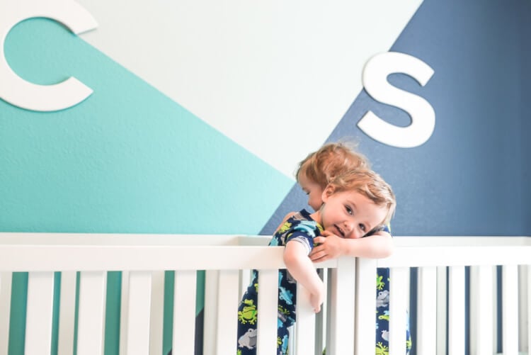 Two little boys in cribs hugging one another and walls painted in dark blue, aqua blue and mint green.  Walls are decorated with the initial\'s \"C\" and \"S\"