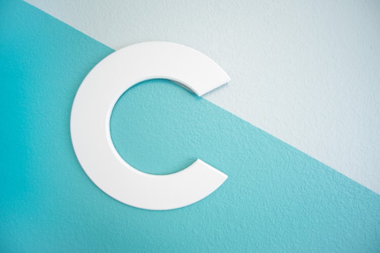 A white letter \"C\" hanging on a wall painted mint green and aqua