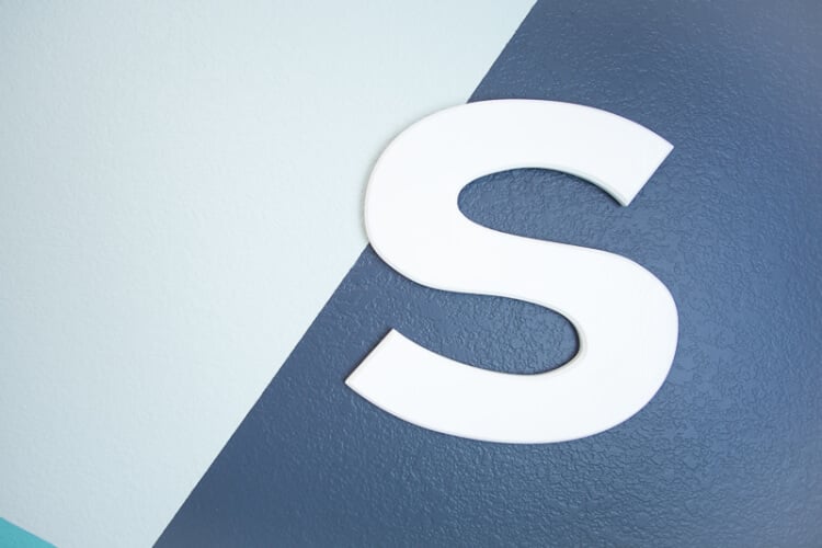 A white letter \"S\" hanging on a wall painted mint green and dark blue