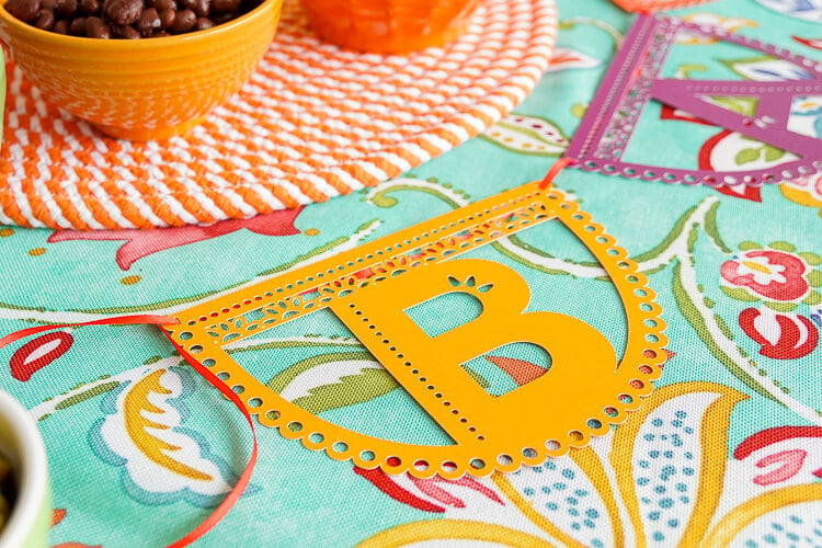 Images of a papel picado letter \"B\" on top of a colorful table cloth