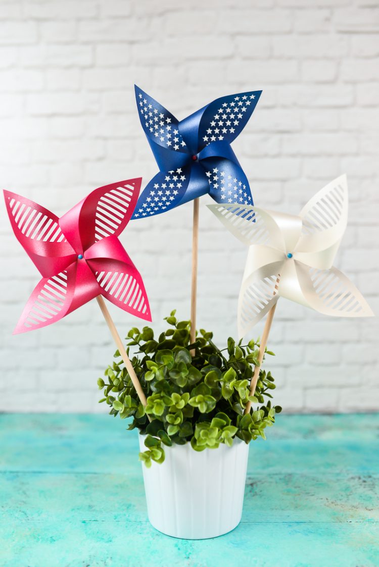 Red, white and blue pinwheels in a potted plant sitting on an aqua blue table against a white brick wall