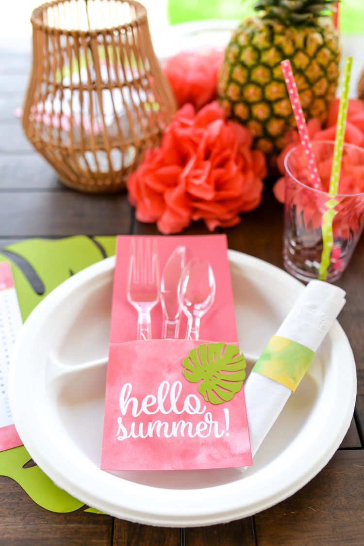 A close up of a table with fruit, flowers and a place setting that contains plastic cutlery wrapped in a utensil holder made from paper cardstock