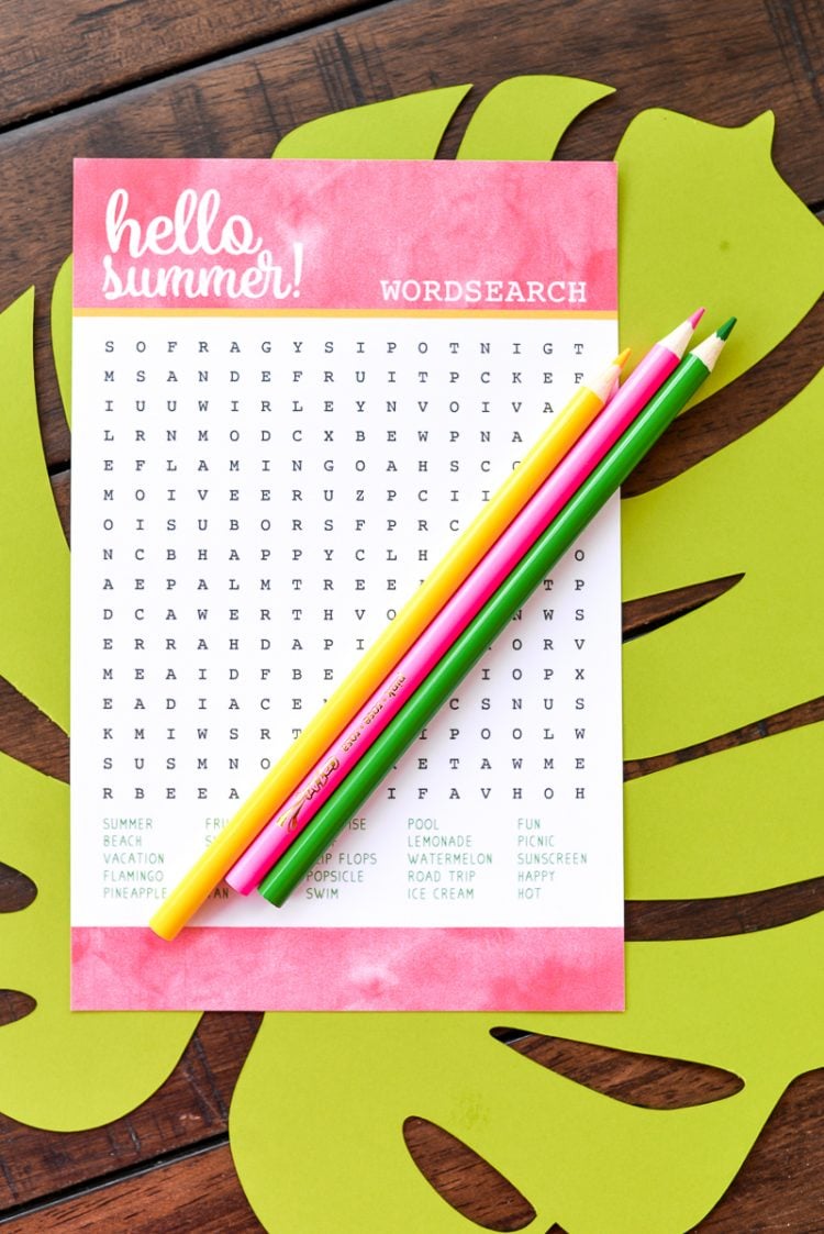 Three pencils and a word search puzzle sitting on top of a large paper cut tropical leaf