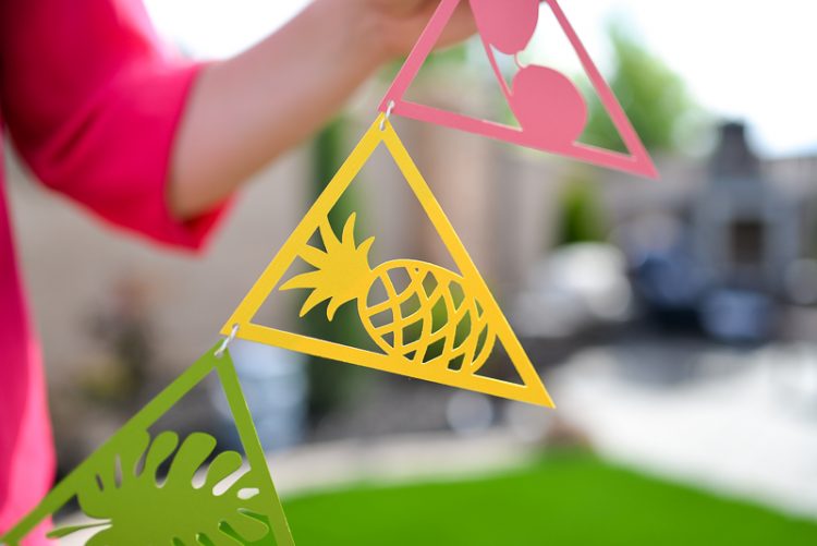 A close up of a woman holding a string of paper cut pennants with a tropical theme