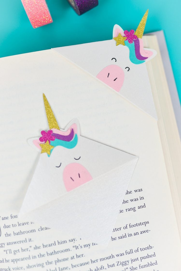 Washi tape next to an open book with two unicorn bookmarks on top of it