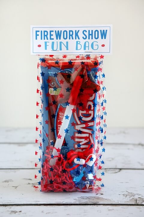 Image of a clear cellophane bag filled with goodies and a tag stapled to the top of the bag that says, \"Firework Show Fun Bag\"