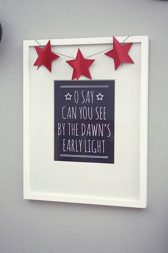 A sign hanging on a wall that says, \"O Say Can You See by the Dawn\'s Early Light\" and is decorated with red stars