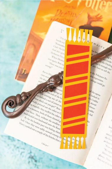 A Harry Potter book underneath of another open book that has a carved stick and a bookmark on top of it