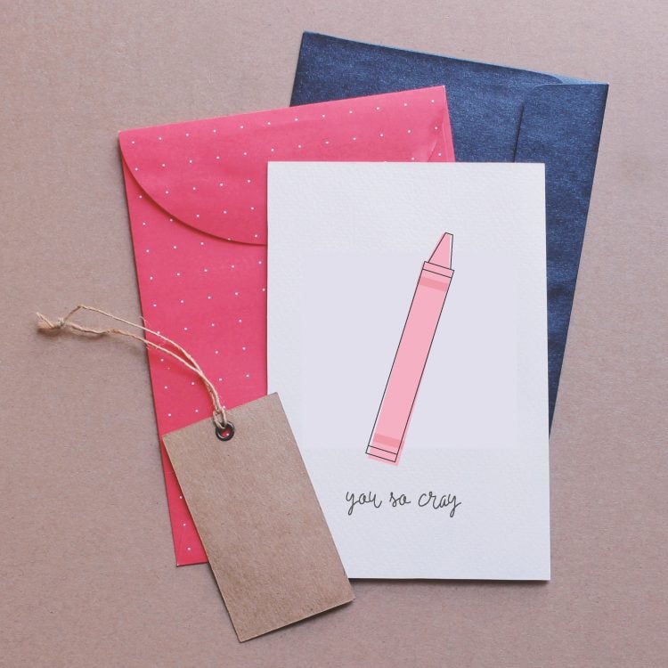 A blue and a pink envelope along with a gift tag and a piece of paper with a pink crayon image on it and the saying, \"You So Cray\"