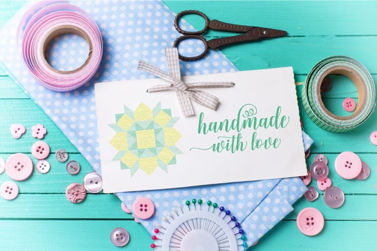 Fabric, scissors, ribbon, pins, buttons and a card tied with a ribbon and says, \"Handmade with Love\"