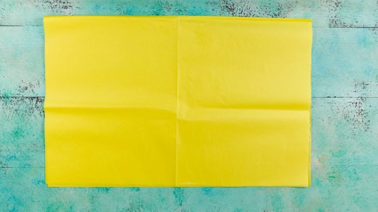 A piece of yellow tissue paper lying on an aqua blue table