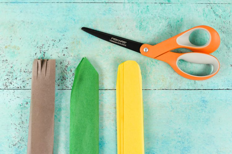 A pair of scissors and yellow, green and brown tissue paper on an aqua blue table