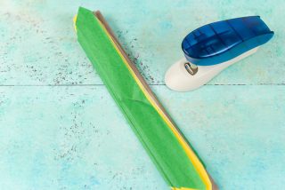 A stapler and brown, yellow and green folded tissue paper laying on an aqua blue table