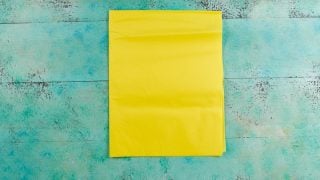 A piece of yellow tissue paper lying on an aqua blue table