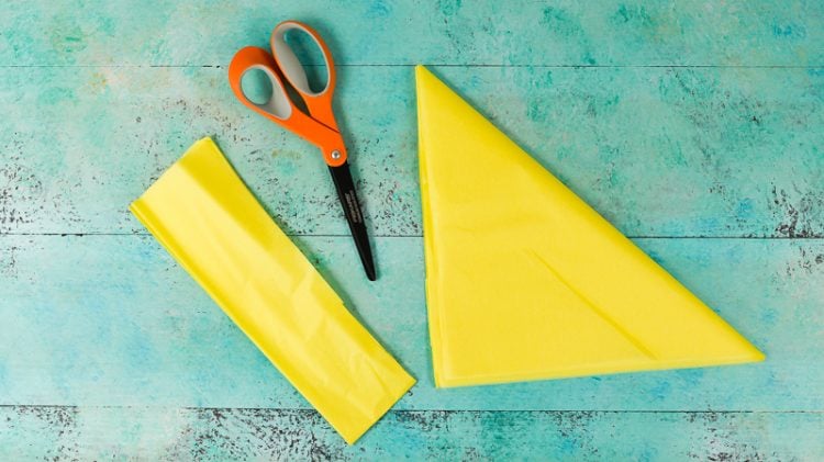 A scissors and two pieces of yellow tissue paper lying on an aqua blue table