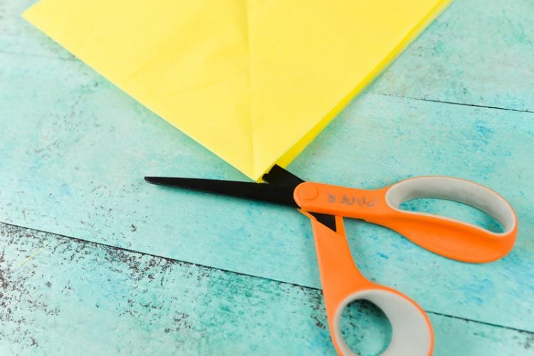 A scissors and a piece of yellow tissue paper lying on an aqua blue table