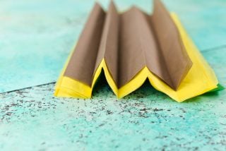 Yellow and brown tissue paper folded in accordion style on an aqua blue table