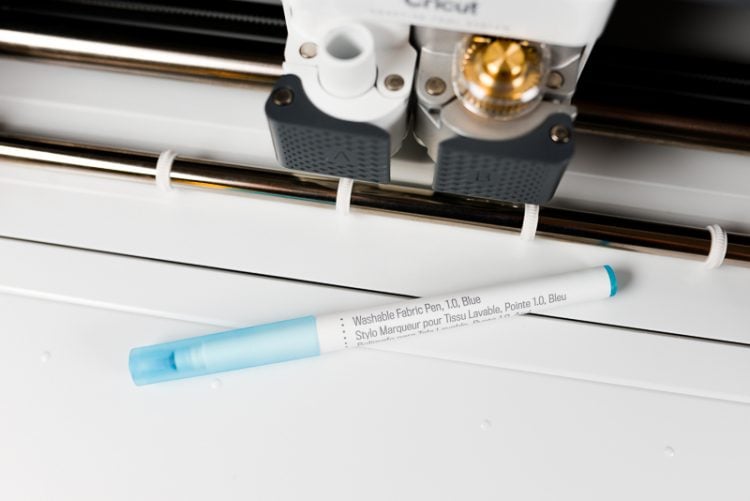 Close up of a Cricut machine with a pen lying by it