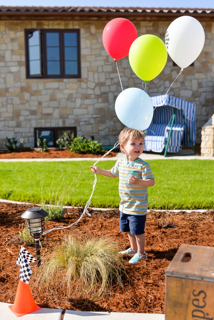 A little boy standing outside holding on to balloons