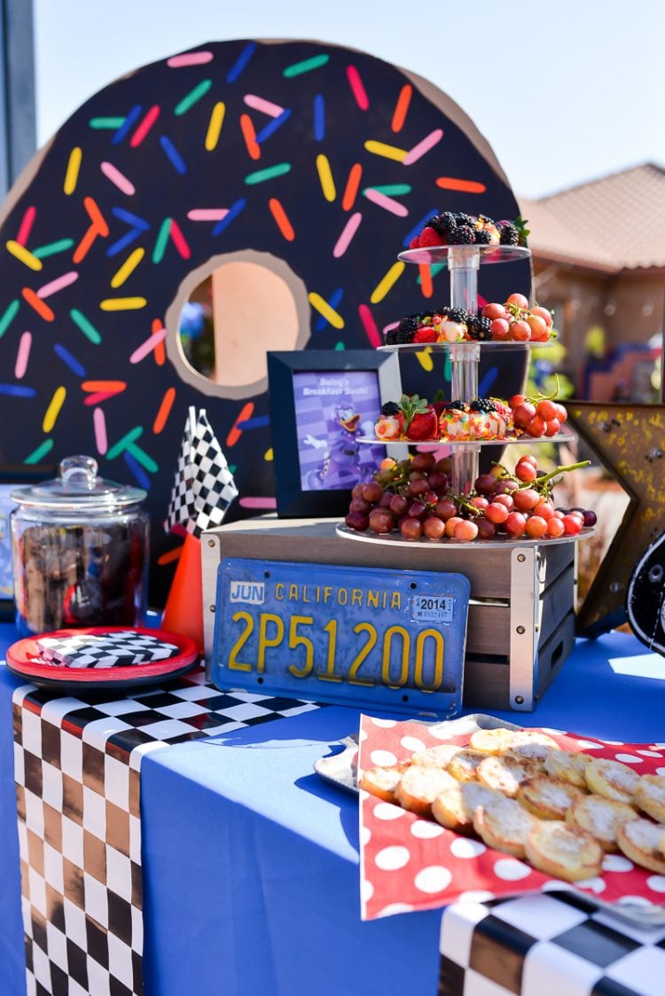 A decorated race car themed table with fruit and sweets on it
