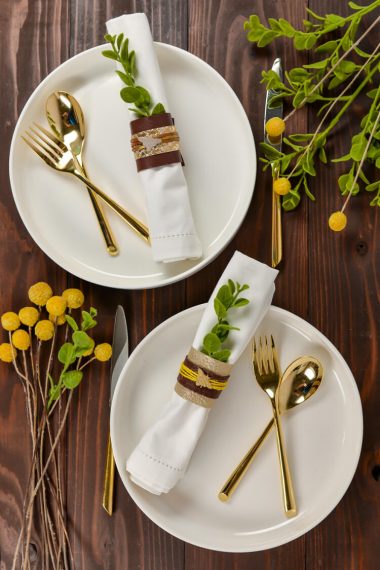 Sprigs of yellow flowers, two place settings of a plate, fork, spoon, and cloth napkins with napkin rings sitting on a table