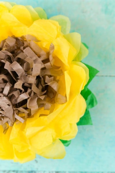 A yellow, green and brown tissue paper sunflower on an aqua blue table