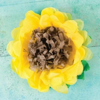 A yellow, green and brown tissue paper sunflower on an aqua blue table