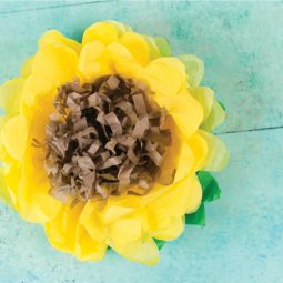 A yellow, green and brown tissue paper sunflower on an aqua blue table