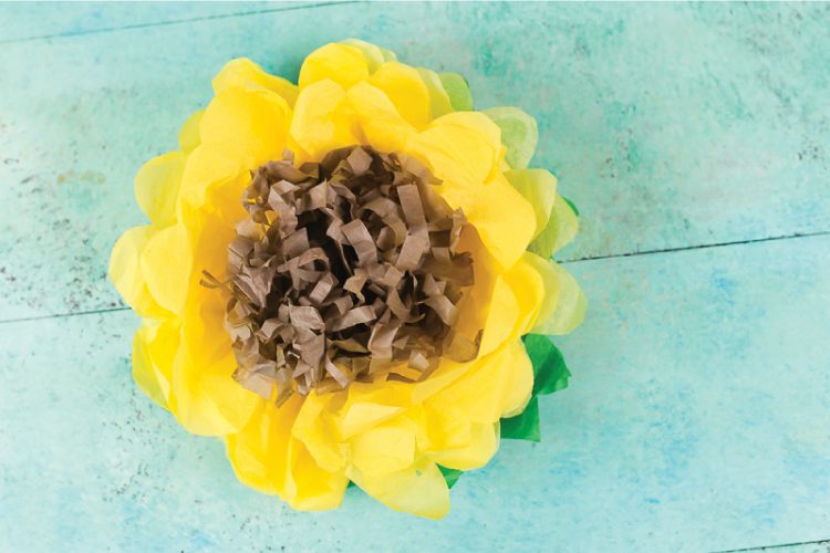 A yellow, green and brown tissue paper sunflower on an aqua blue table