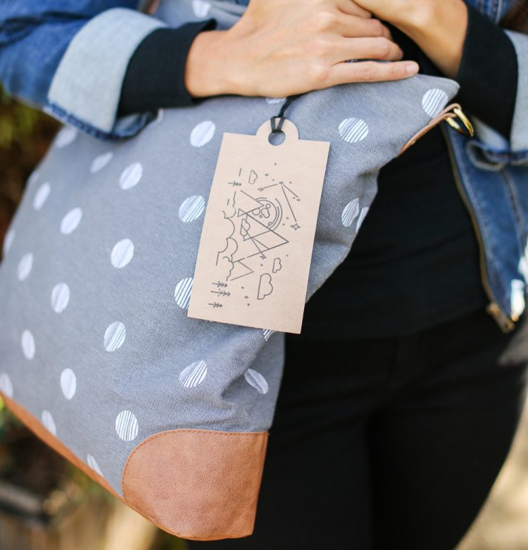 A close up of a woman holding a blue polka dot purse that has a tag hanging from it