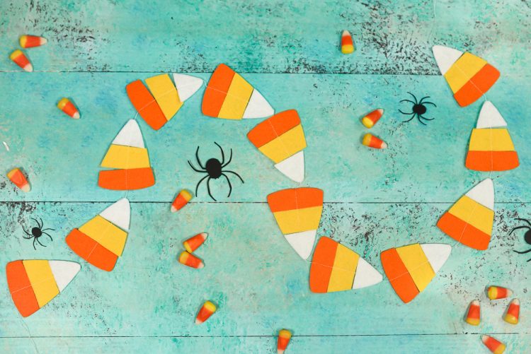 Real candy corn candy, paper cut black spiders and a candy corn garland lying on an aqua blue table