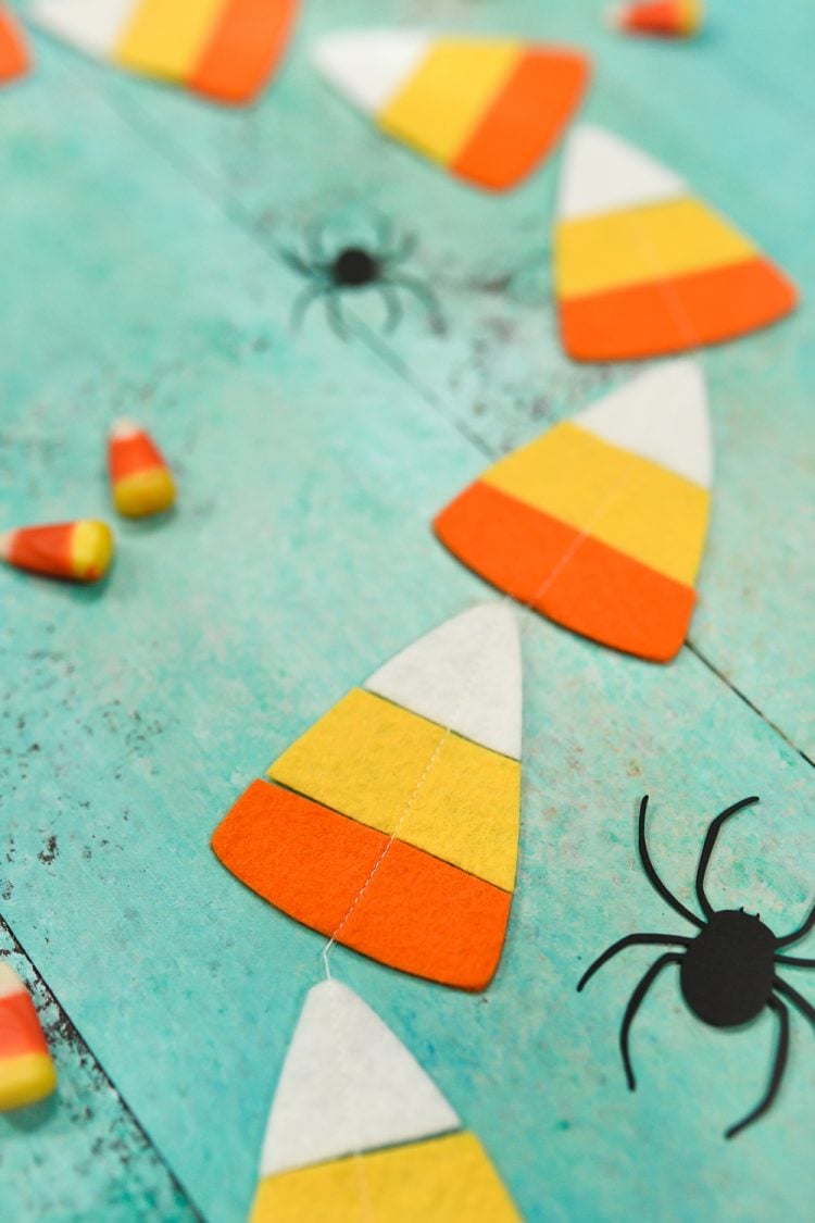 CLose up of real candy corn candy, paper cut black spiders and a candy corn garland lying on an aqua blue table