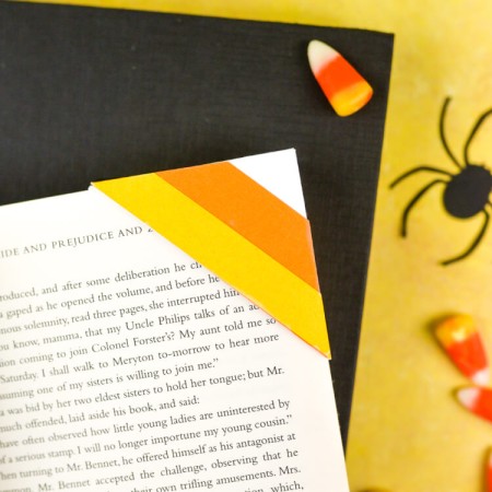 Candy corn candy, a black paper cut spider and a book with a white, orange and yellow candy corn candy bookmark