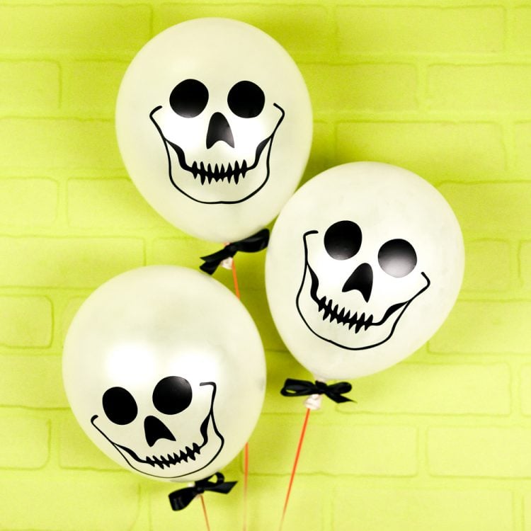 Against a lime green wall are three white balloons decorated with skulls