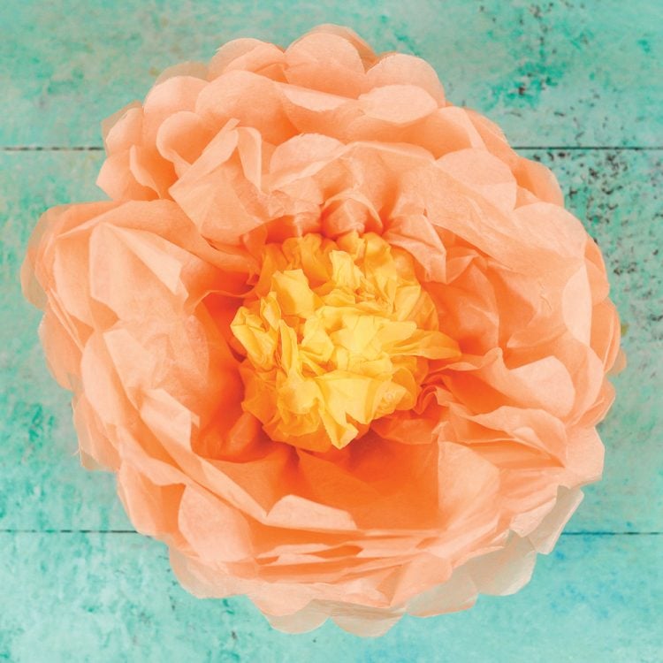 Close up of an orange and yellow paper tissue flower against an aqua background