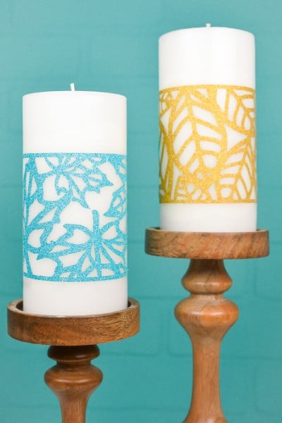 Two white candles in wooden candle holders and decorated with an aqua and a gold fall leave wrap