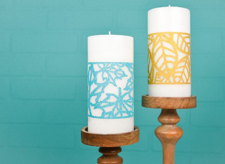 Two white candles in wooden candle holders and decorated with an aqua and a gold fall leave wrap